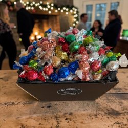 Luksuschokolade til jul og store decemberhilsner: Stemningsfuldt vinters�sonbillede af den fyldige chokoladesammens�tning, anrettet dekorativt i butikken ved siden af et flot, pyntet juletr� med glitrende lys.