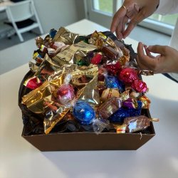 Gavekurv som julehilsen eller mindre firmagave: Stemningsfuldt produktbillede af den �bne chokoladegave, fotograferet t�t p� under de gyldne og glitrende lysk�der i butikkens udstilling