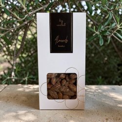 L�kre saltede og r�gede mandler i gave�ske: Indbydende produktbillede af den lukkede snack�ske, anrettet dekorativt i butikken ved siden af en udsk�ret figur af et mandeltr�.